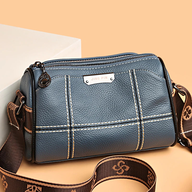A dark blue leather shoulder bag with gold stitching and a brown strap resting on a light background.