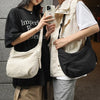 A person is holding a beige soft nylon crossbody shoulder bag while wearing a black top and light colored vest.
