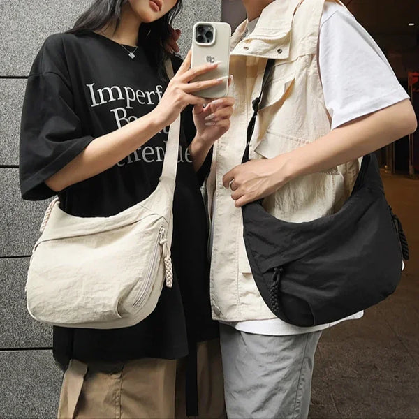 A person is holding a beige soft nylon crossbody shoulder bag while wearing a black top and light colored vest.