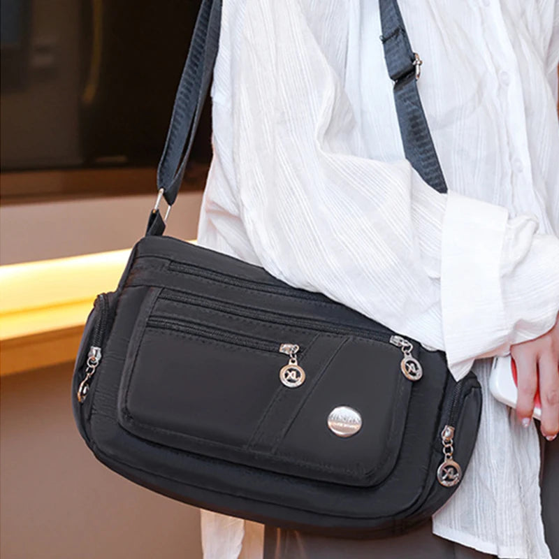 A black waterproof nylon crossbody tote bag being held by a person wearing a white shirt.