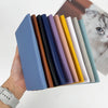 A hand holds a colorful set of customizable PU leather passport holders with various shades of blue, brown, purple, yellow, a