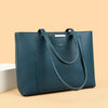 A dark teal leather shoulder bag with a gold-tone hardware resting on a light beige surface.