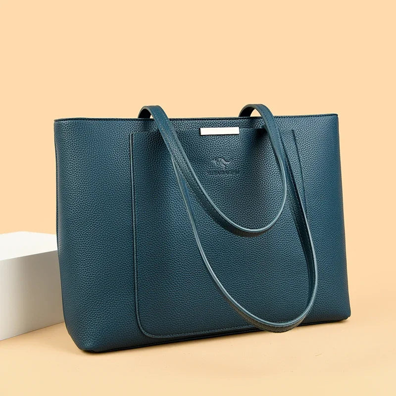 A dark teal leather shoulder bag with a gold-tone hardware resting on a light beige surface.