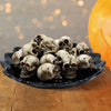 Pila de esculturas de cráneo de resina realista para decoración de Halloween, expuestas en un plato negro.