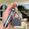 A black silicone heart beach bag keychain with a gold-colored metal loop is held in a hand.