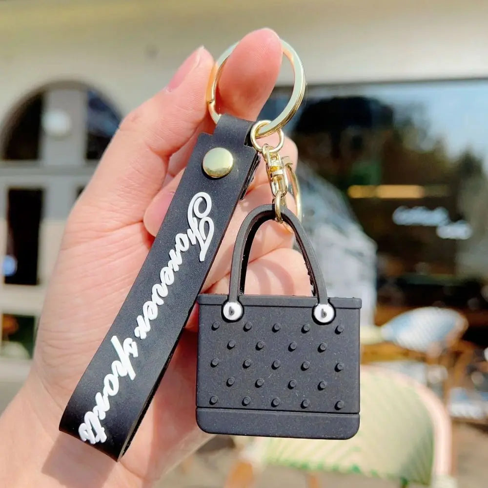 A black silicone heart beach bag keychain with a gold-colored metal loop is held in a hand.
