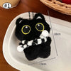 Un peluche de gato negro con ojos amarillos y una bufanda blanca a rayas, exhibido en un plato blanco.