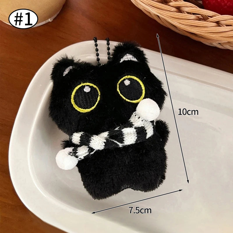 Un peluche de gato negro con ojos amarillos y una bufanda blanca a rayas, exhibido en un plato blanco.
