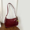 A maroon PU leather shoulder bag with a gold cherry pendant hanging against a white wall.