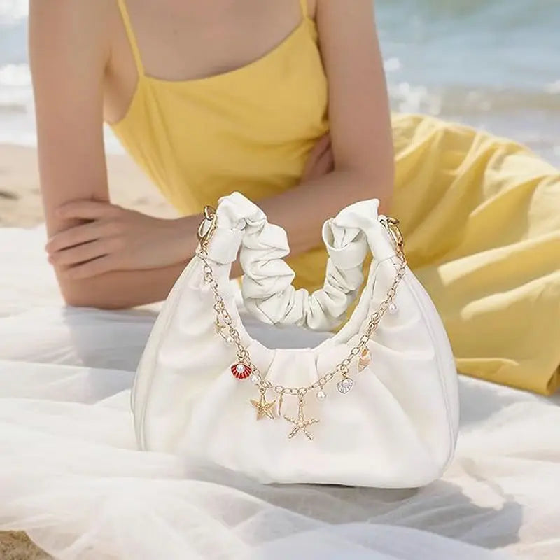 A white elegant metal bag with gold charms and keychains resting on a white fabric near the ocean.