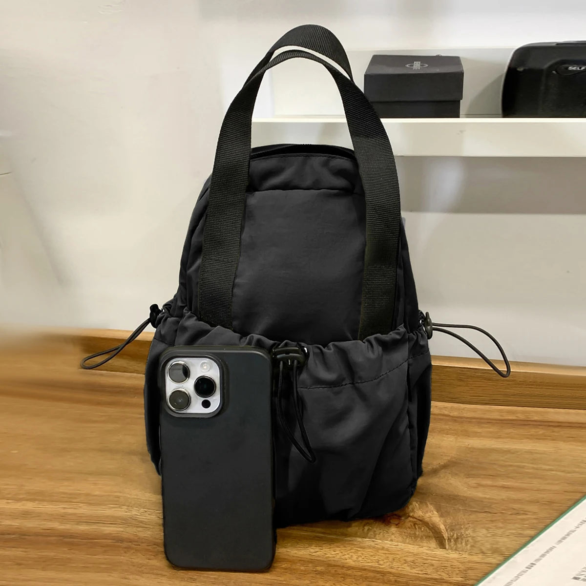 A black casual backpack with a laptop compartment and a smartphone attached, resting on a wooden surface.