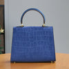A deep blue crocodile pattern tote bag with a leather handle resting on a wooden table.