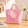 A pink and white striped waterproof PVC shoulder tote bag resting on a wooden table next to a cup and some books.