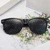A pair of black precision vision correction glasses resting on a white surface with greenery.