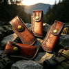 A close-up of a brown leather knife sheath with a belt loop and brass button resting on dark rocks.