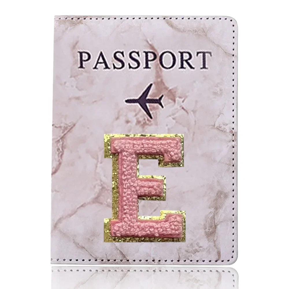 Cubierta de pasaporte de mármol rosa con una letra E grabada en oro y un ícono de avión negro.