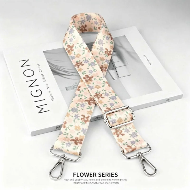 A beige floral patterned nylon shoulder strap with a silver buckle displayed on a white box.