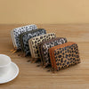 A collection of leopard print double zipper wallets displayed on a wooden surface.