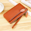 A brown genuine leather wristlet clutch wallet with a zipper closure resting on a wooden surface.
