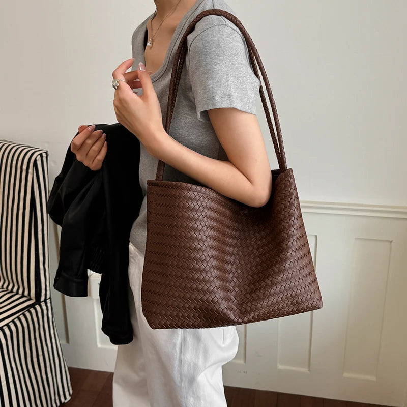 A person holds a brown crocodile-textured PU bucket shoulder bag against a gray t-shirt.