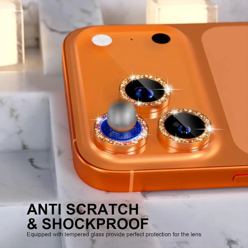 An orange glitter diamond camera lens protector with a metal frame for an iPhone is shown on a marble surface.