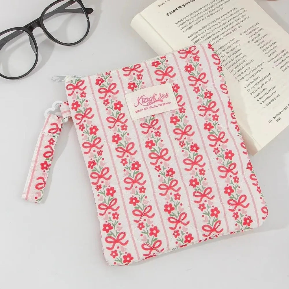 A pink and white floral plaid cotton tablet pouch with a pink ribbon closure resting on a white surface.