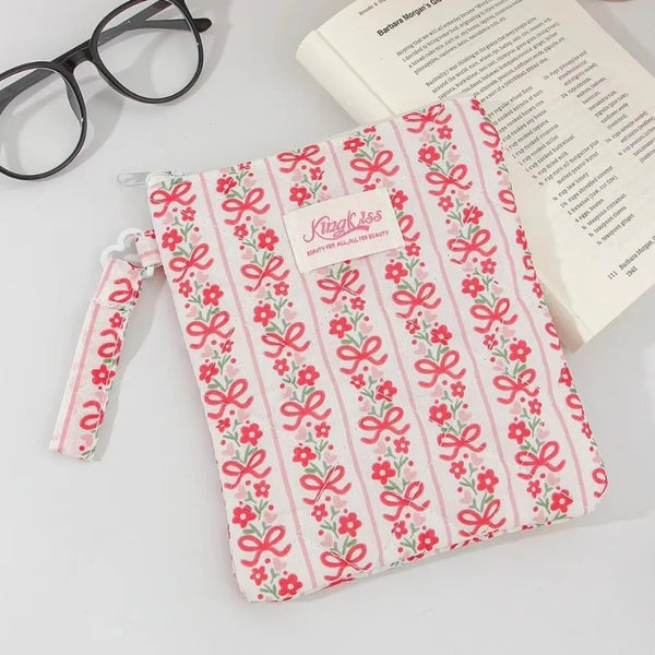 A pink and white floral plaid cotton tablet pouch with a pink ribbon closure resting on a white surface.