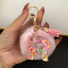 A hand holds a custom initial letter keychain featuring a shiny resin pendant and pink alphabet charm.