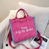 A pink tote bag with blue trim is displayed on a white textured surface.