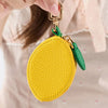 A close-up of a yellow coin purse keychain with a textured surface and green fabric detail being held by a hand.