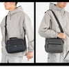 A man wears a gray waterproof jacket with a black crossbody messenger bag attached to the side.