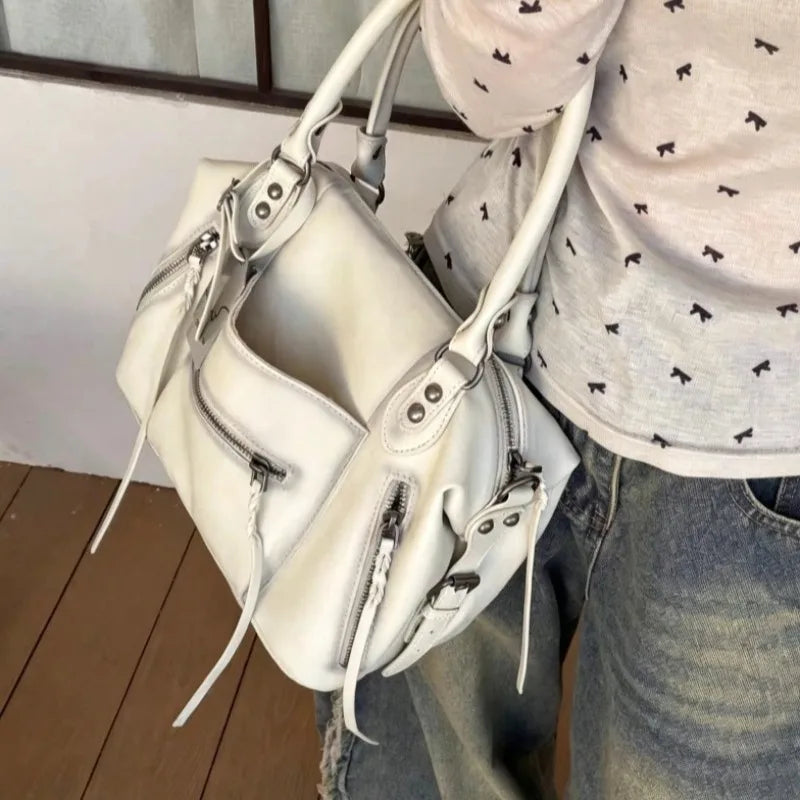 A white vintage PU leather crossbody tote bag with adjustable straps being held by a person.