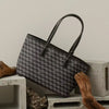 A dark gray geometric patterned tote bag with leather handles resting on a light-colored wooden surface.