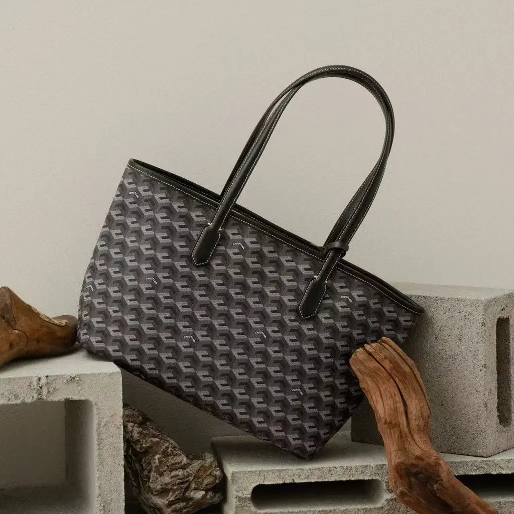 A dark gray geometric patterned tote bag with leather handles resting on a light-colored wooden surface.