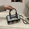 A dark brown crossbody bag featuring a piano print and checkered fabric accents, held by a hand.