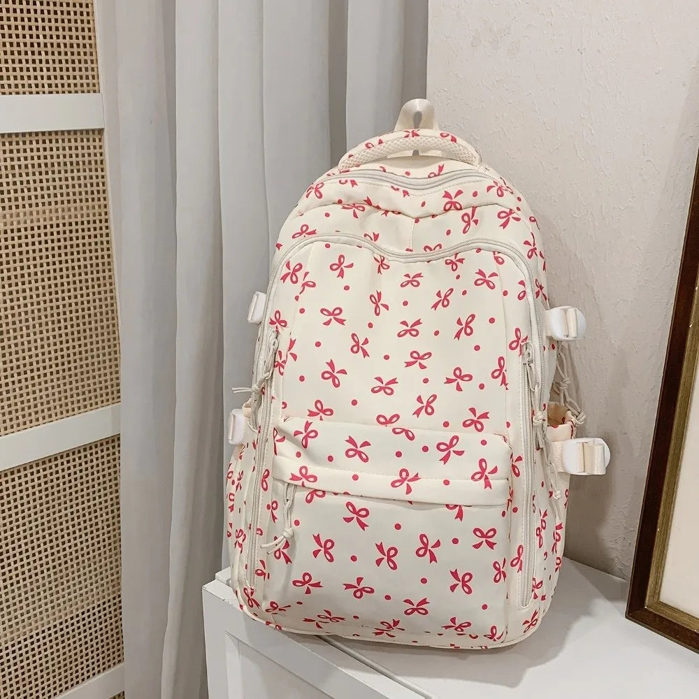 Mochila blanca con estampado floral de flores rosas y rojas, mostrada sobre fondo claro.