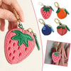 Eine Hand hält eine rosa Erdbeere-Charm-Münztasche als Schlüsselanhänger mit grünem Blattdetail und mehreren Frucht-Charms.