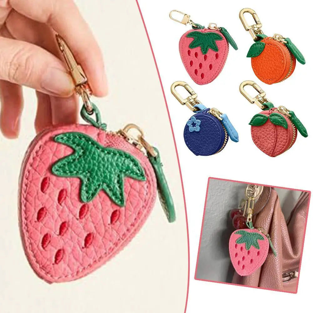 Eine Hand hält eine rosa Erdbeere-Charm-Münztasche als Schlüsselanhänger mit grünem Blattdetail und mehreren Frucht-Charms.