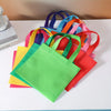 A colorful display of non-woven tote bags in various shades including yellow, green, orange, pink, and purple.
