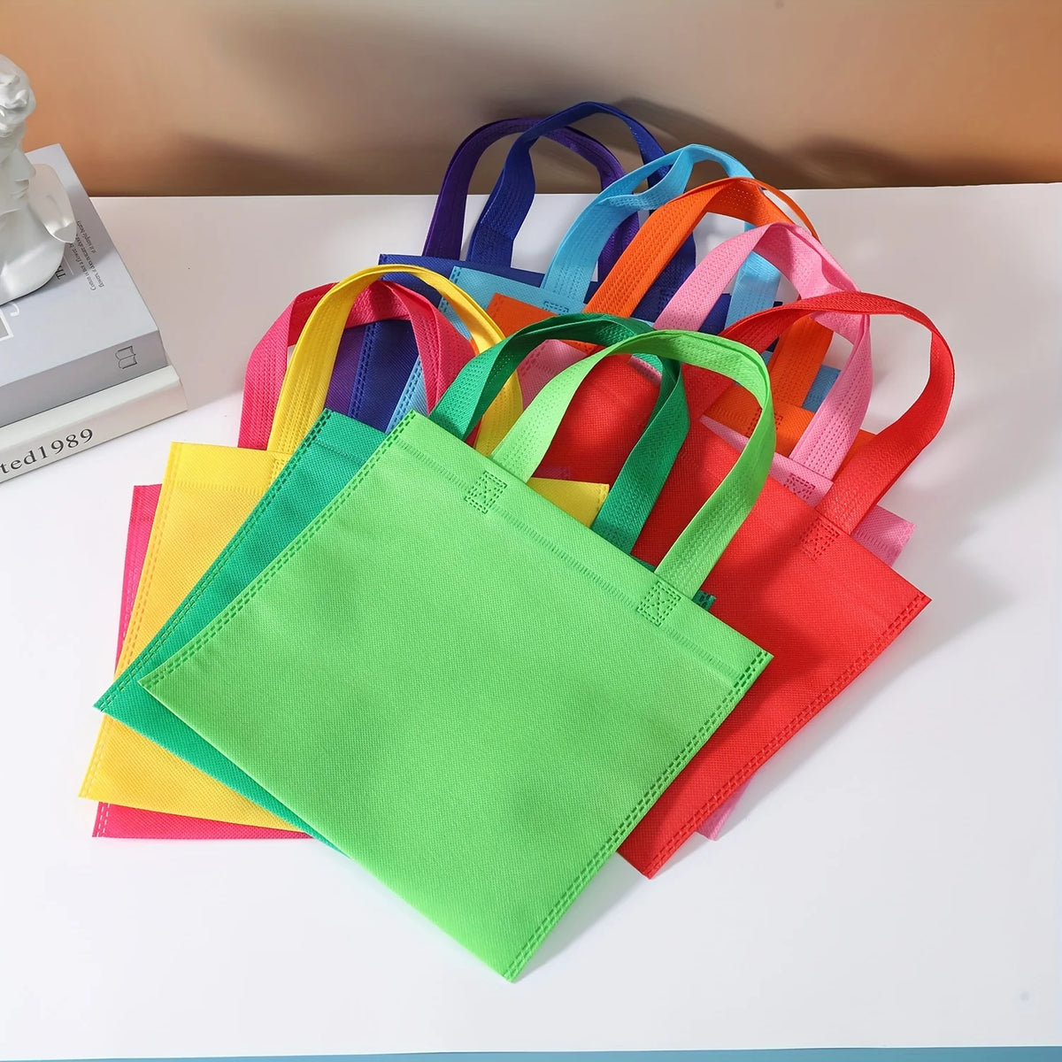 A colorful display of non-woven tote bags in various shades including yellow, green, orange, pink, and purple.