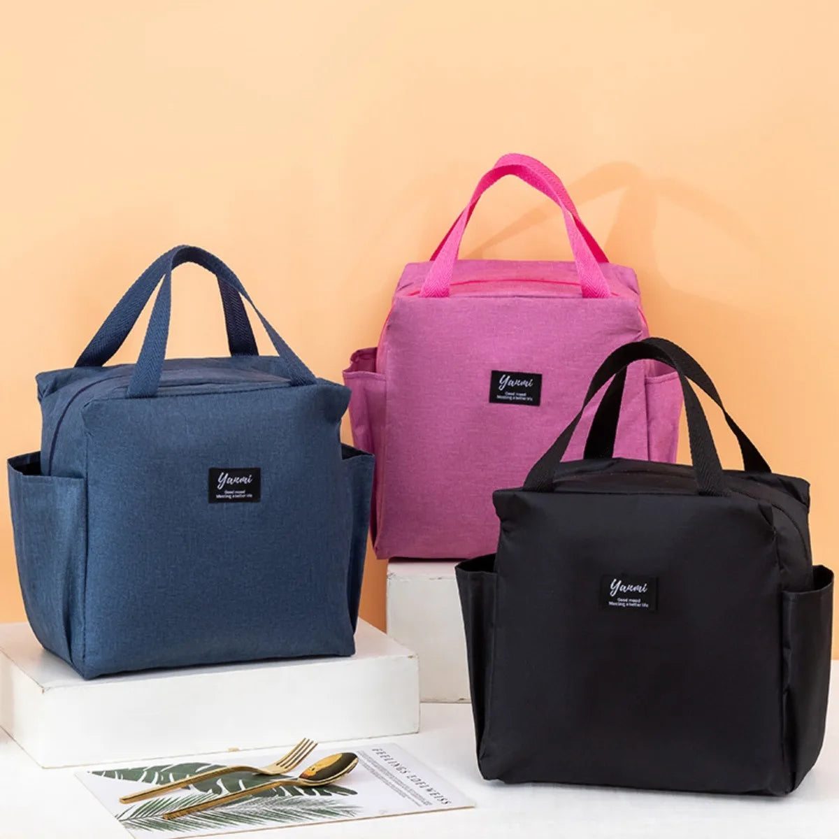 Three insulated canvas tote bags in navy blue, pink, and black are displayed on a white surface.