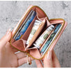 A hand holds an open pink cartoon mini zipper coin purse filled with rolled-up US dollar bills.