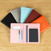 A collection of slim passport holders in various colors including black, gray, light blue, and orange resting on a wooden sur