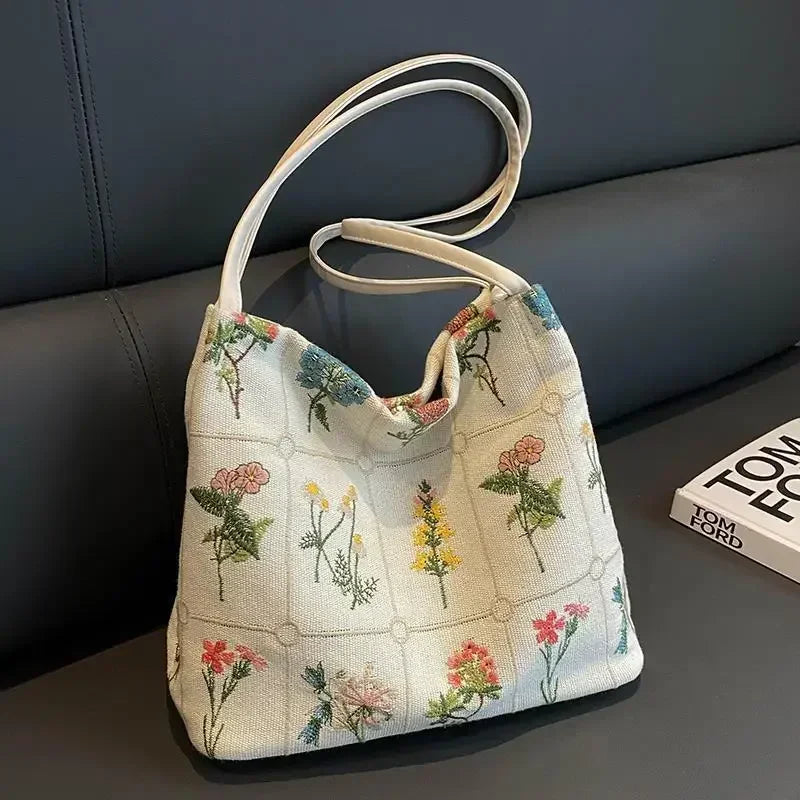 Bolso de seda jacquard beige claro con bordado floral y correas de cuero blanco sobre una superficie oscura.