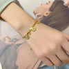 A close-up of a gold stainless steel charm bracelet with portrait pendants worn on a wrist.