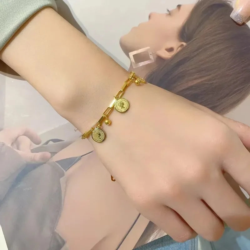 A close-up of a gold stainless steel charm bracelet with portrait pendants worn on a wrist.