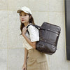 A young woman wearing a white cap and beige outfit holds a brown leather shoulder bag.