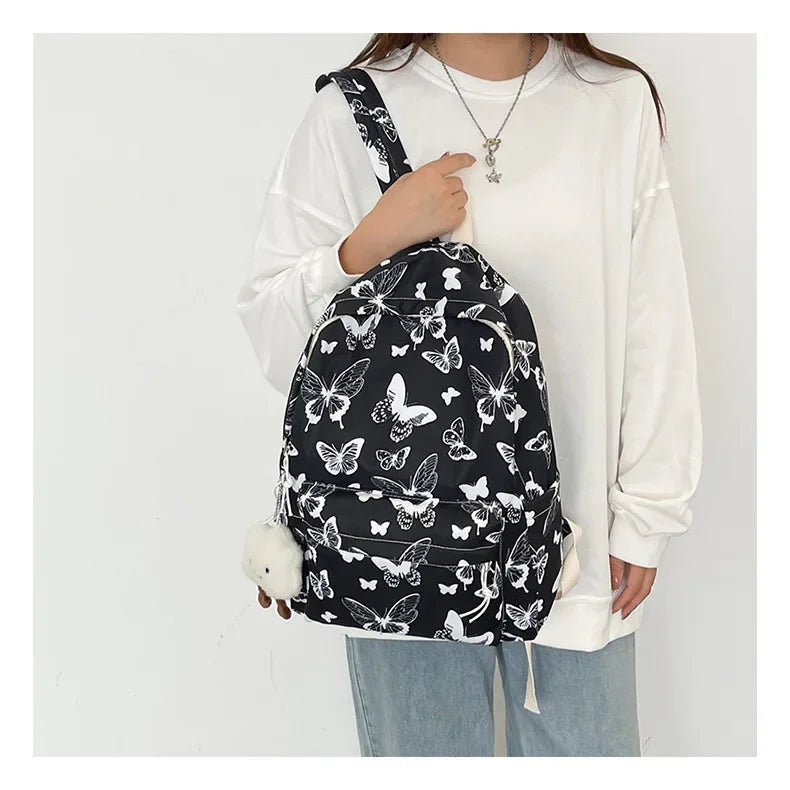 A woman is wearing a black backpack with a white butterfly pattern and a white long-sleeved shirt.