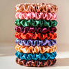 A stack of 19 thin scrunchies hair ties in various satin colors including pink, green, purple, orange, blue, and brown.
