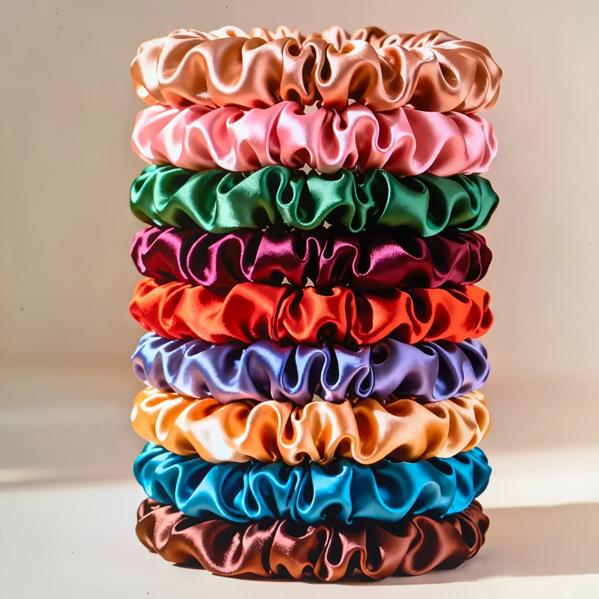 A stack of 19 thin scrunchies hair ties in various satin colors including pink, green, purple, orange, blue, and brown.